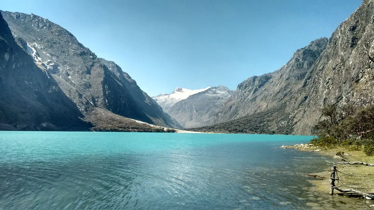 Turquoise water of a Llanganuco lake between rock walls and a snow-capped peak